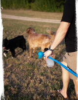 a man walking holding a dog tennis ball launcher with a carbon hound frag munch GLOW dog toy in it, with dogs seen blurred in the background